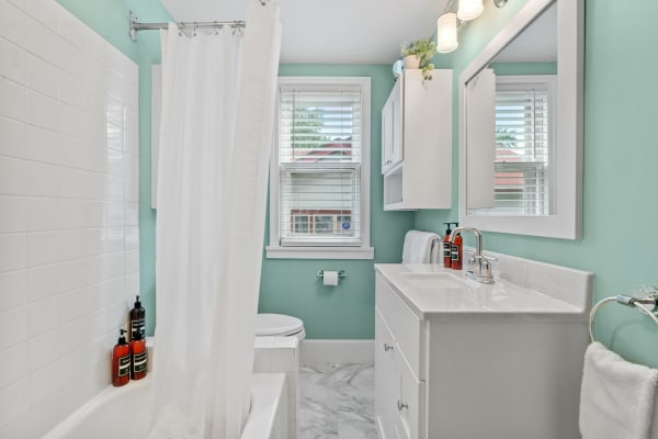 Modern bathroom featuring turquoise walls, white tiled bathtub, and double sink vanity.