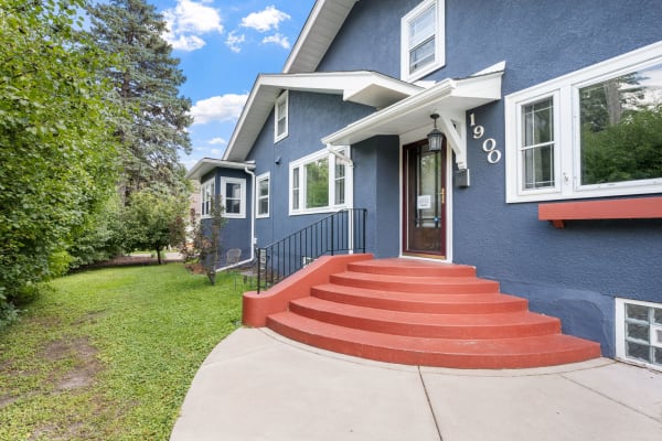 Front view of a blue house with red steps surrounded by greenery.