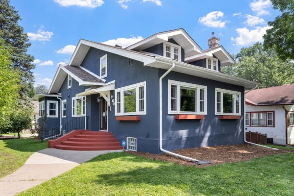 A blue house with red steps and large windows, set against a green lawn and blue sky.