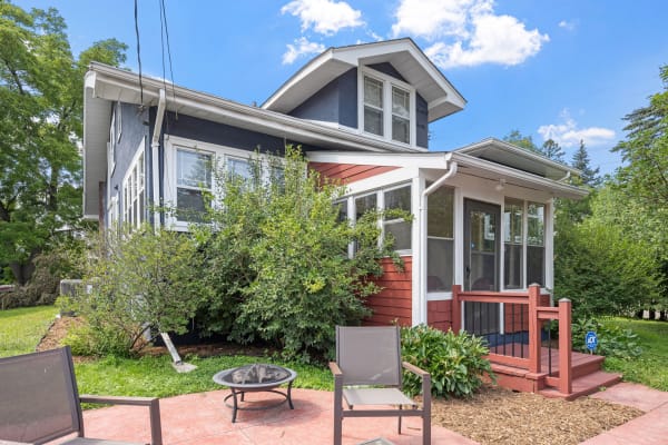 A charming house with blue exterior and red accents, surrounded by greenery and outdoor seating.