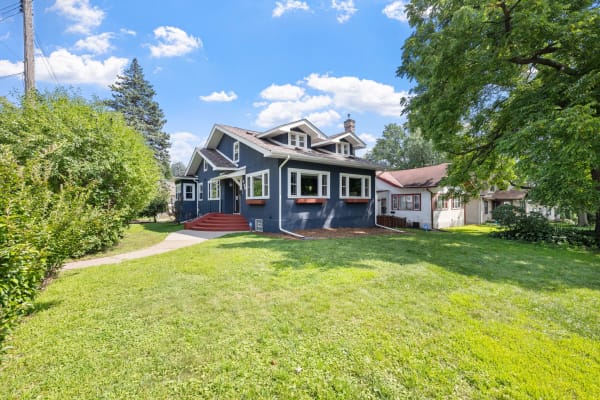 A blue house with white trim and red steps surrounded by green grass and trees.