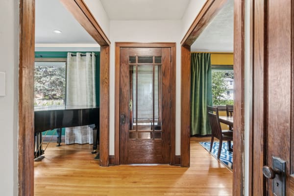 A cozy entryway showing a wooden door, grand piano, and dining area with green curtains.