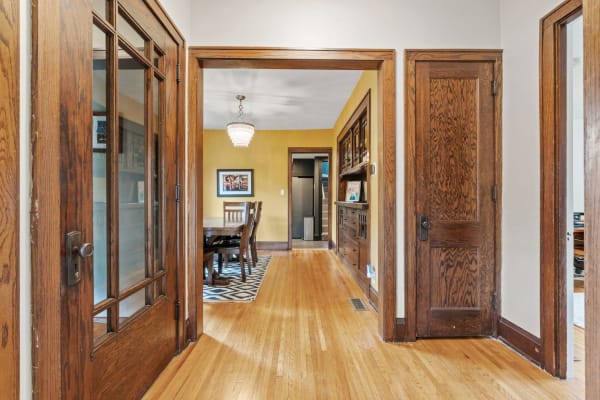 A cozy hallway with wooden doors leading to a dining room adorned with a chandelier.