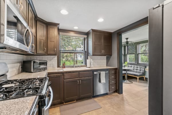 A contemporary kitchen featuring dark wooden cabinets, granite countertops, and a dining nook with a black tufted bench.