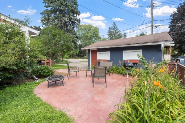 Outdoor patio with chairs, a fire pit, and flowers; blue building in the background.