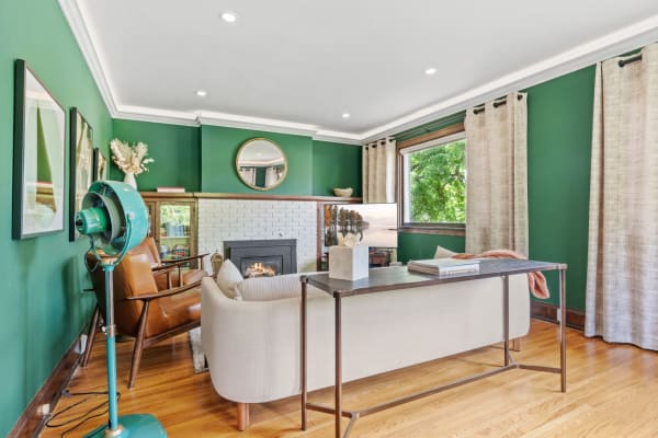 A stylish living room featuring green walls, a beige sofa, brown leather chair, and a turquoise fan.