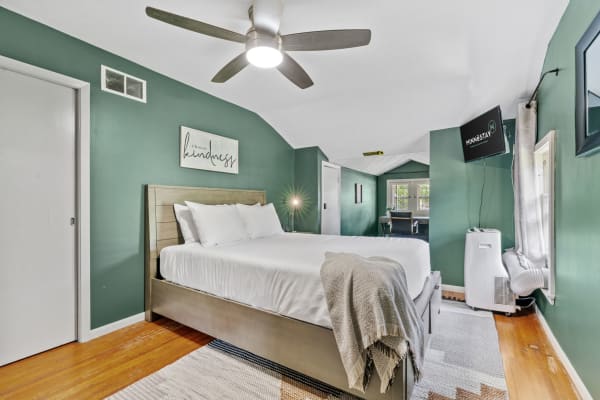 Modern bedroom with a green accent wall, a queen bed, and a writing desk.