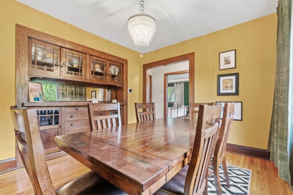 A rustic dining room with a wooden table, chairs, and a crystal chandelier against yellow walls.