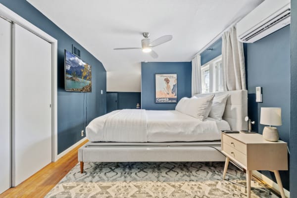 A modern bedroom with blue walls, light bedding, a TV, and stylish decor.