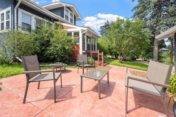 Outdoor patio with gray chairs and glass-topped table set against a residential house.