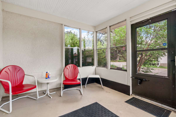 Cozy porch with red chairs, a round table, and bottles of sunscreen.