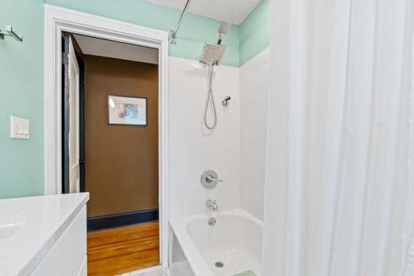 Modern bathroom with mint green walls, white tiles, and a tub with a showerhead.