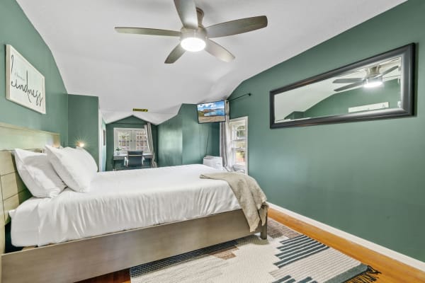 A modern bedroom featuring green walls, a bed with white linens, and a desk area by a window.