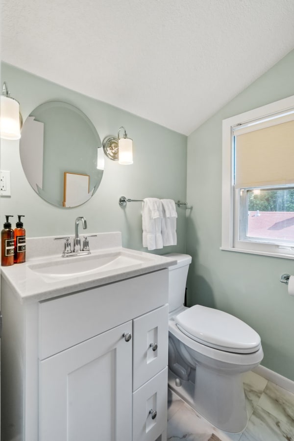 Modern bathroom with green walls, white vanity, and natural lighting.