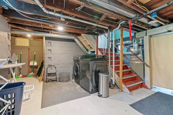 Basement laundry area with washing machine, cleaning supplies, and stairs.