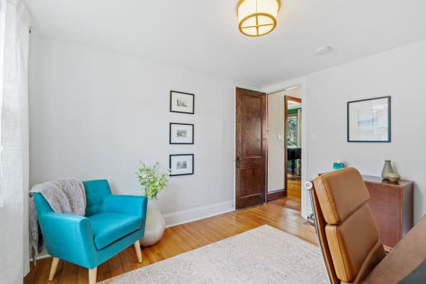 Cozy home office featuring a turquoise chair, wooden flooring, and framed artwork.
