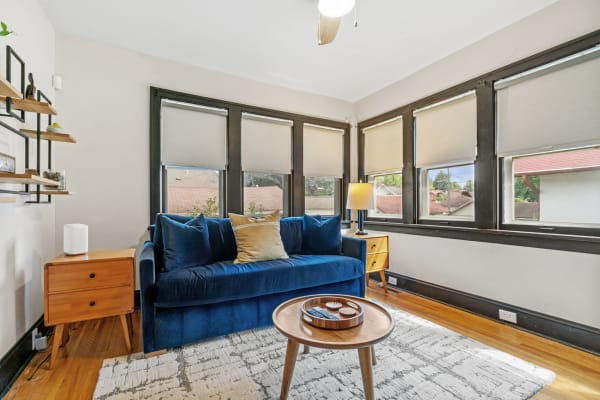 Cozy living room with blue velvet sofa and wooden details next to large windows.