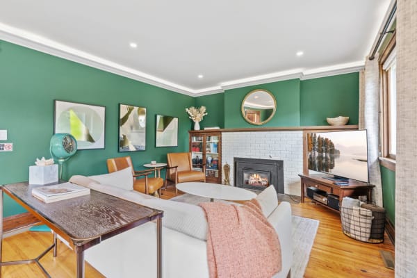 A stylish living room featuring a green wall, brown chairs, and a white brick fireplace.