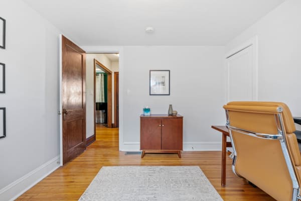 A cozy room with wooden accents, featuring a cabinet, a stylish chair, and an open door to another room.
