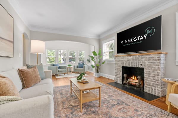 Modern living room with a cream sofa, green chairs, and a brick fireplace.