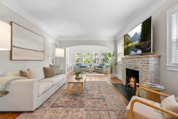 Bright living room with a neutral palette, featuring a sofa, coffee table, fireplace, and large windows.