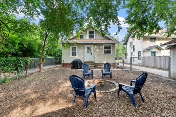A backyard featuring a fire pit surrounded by blue chairs and a house in the background.