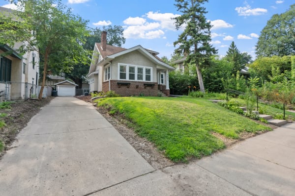 A residential bungalow with a green lawn and driveway leading to a garage.