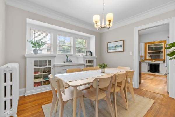 A well-lit dining room featuring a wooden table and light-colored chairs.