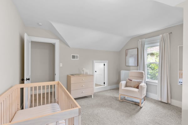 A softly colored nursery room with a wooden crib, dresser, and rocking chair.