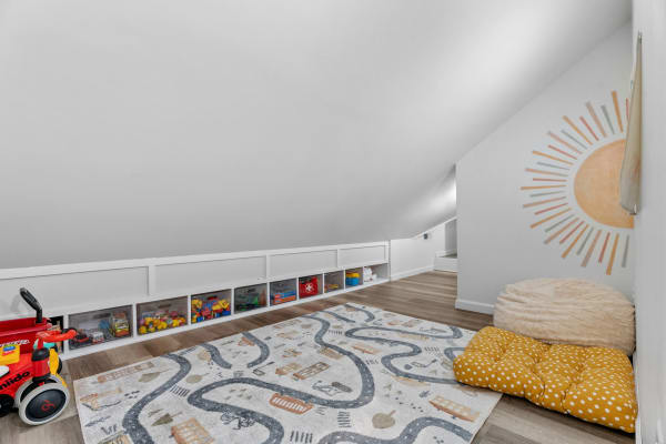 A cozy attic playroom featuring a slanted ceiling, colorful bins, a playful rug, and comfortable seating.