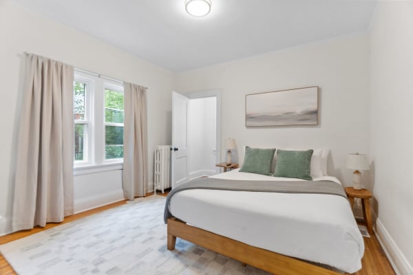 A cozy bedroom featuring a bed with green pillows, soft natural light, and minimalist decor.