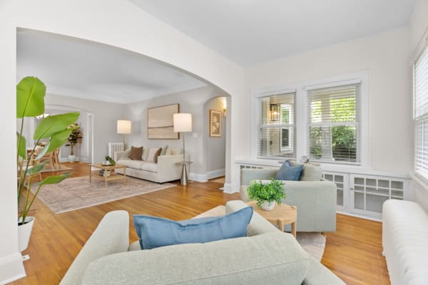 A stylish living room featuring green sofas, a wooden coffee table, and large windows with sunlight.