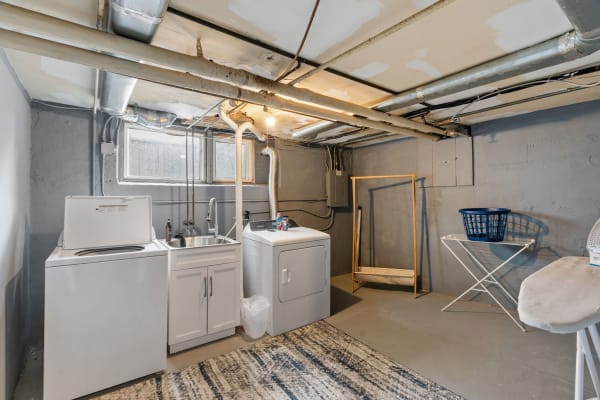 Basement laundry room showcasing a washing machine, dryer, utility sink, and drying area.