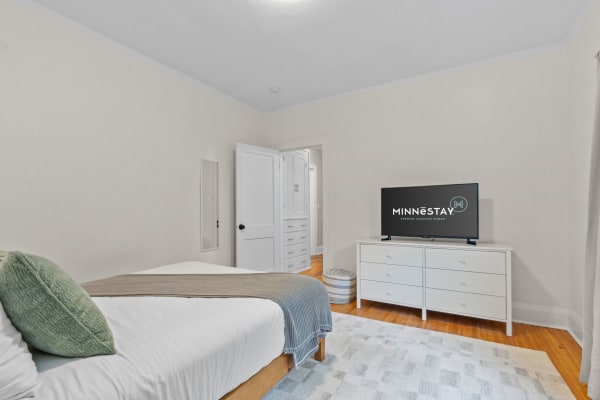A cozy bedroom featuring a white bed with green accents and a television on a white dresser.
