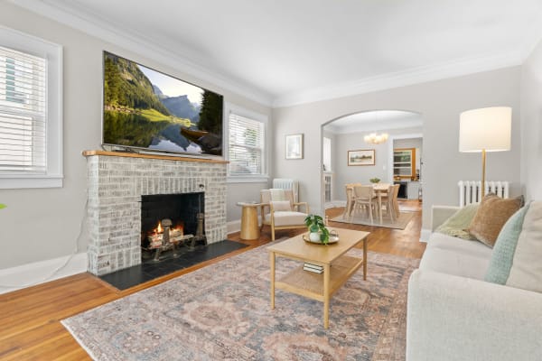 A warm living room with a sofa, coffee table, fireplace, and a wall-mounted TV showing a nature scene.