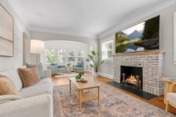 A bright living room with a fireplace, soft seating, and a TV displaying a mountain landscape.