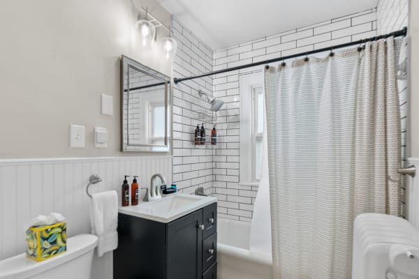 A clean and modern bathroom with black vanity, white tiles, and striped shower curtain.