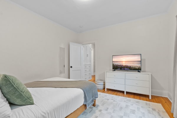 A serene bedroom with a bed, dresser, and TV showing a sunset.