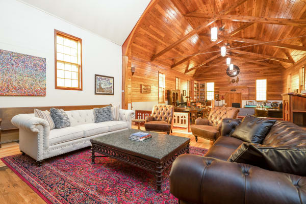A spacious living room featuring a white Chesterfield sofa, dark leather couch, a decorative coffee table, and vibrant artwork on the walls.