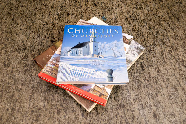Stack of books including "Churches of Minnesota" on a dark stone surface.