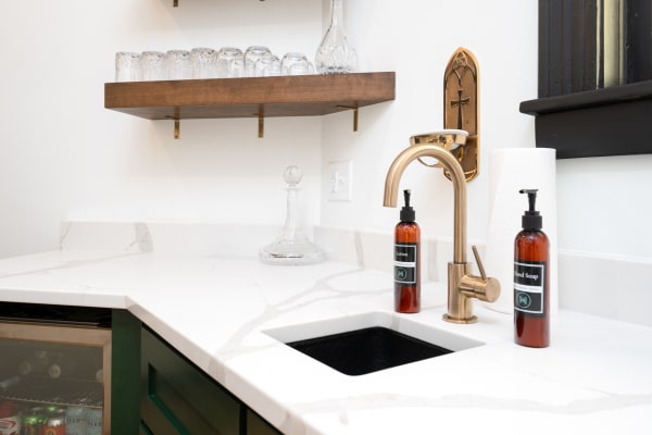 Modern bathroom countertop featuring a gold faucet, amber soap bottles, and glassware.
