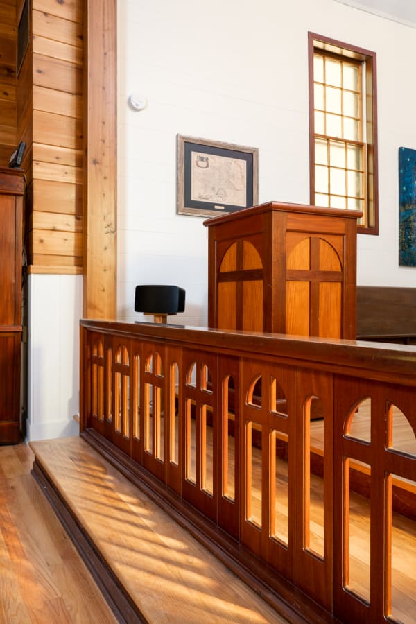 Wooden interior featuring a podium, detailed railing, and artworks with soft light streaming through a window.
