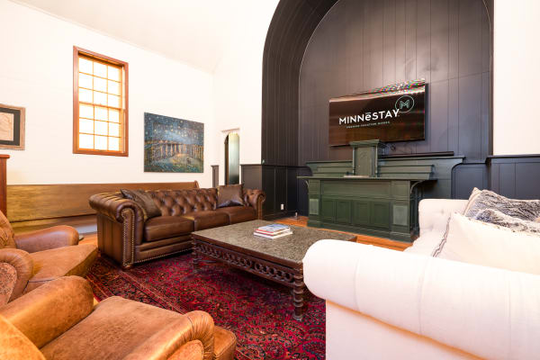 A cozy living room with leather sofas, an ornate coffee table, a vibrant rug, and a wall-mounted TV.