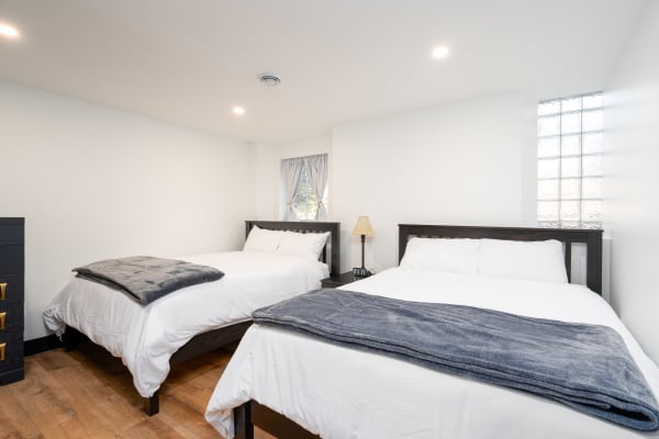 A modern bedroom with two beds, bright white walls, and a soft blue-gray blanket on each bed.