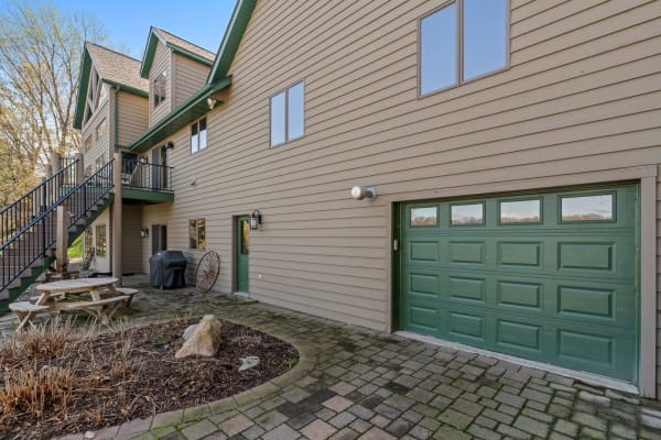 Exterior view of a beige house with green accents, picnic table, and garage.