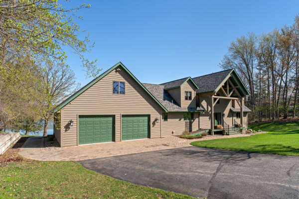 Exterior view of a house with beige siding, green trim, and a lush lawn under a clear blue sky.