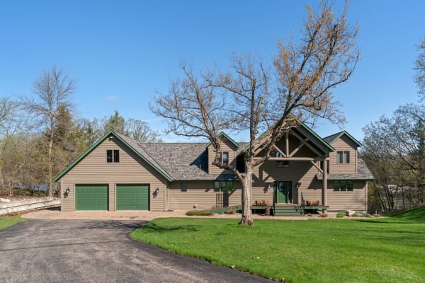 Modern house with beige siding and green trim, featuring a circular driveway and surrounded by trees.
