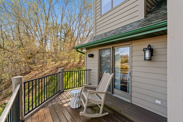 Wooden deck with a rocking chair, small table, and trees in the background.