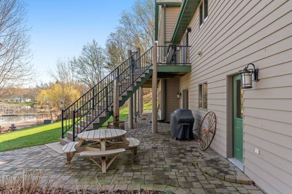 Outdoor patio area with a picnic table, grill, and stairs to the upper level of a home near a waterway.