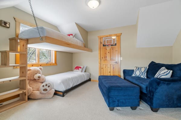 Cozy children's bedroom with a loft bed, teddy bear, and a navy blue couch.